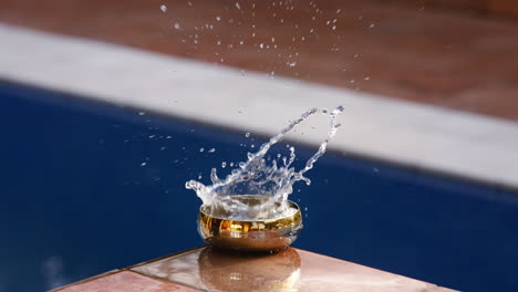 water slashing in slow-motion in a small golden bowel at the edge of a pool