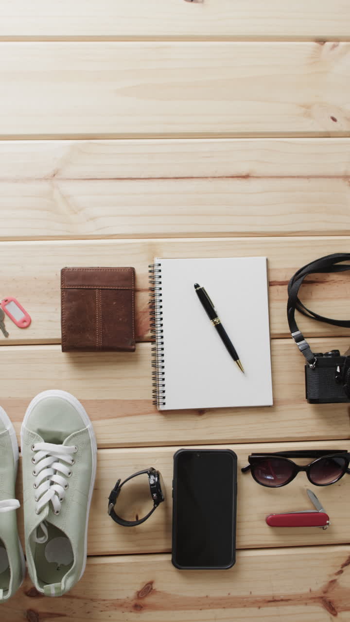 Vertical video of travel items, notebook, smartphone, camera and passport on wooden background