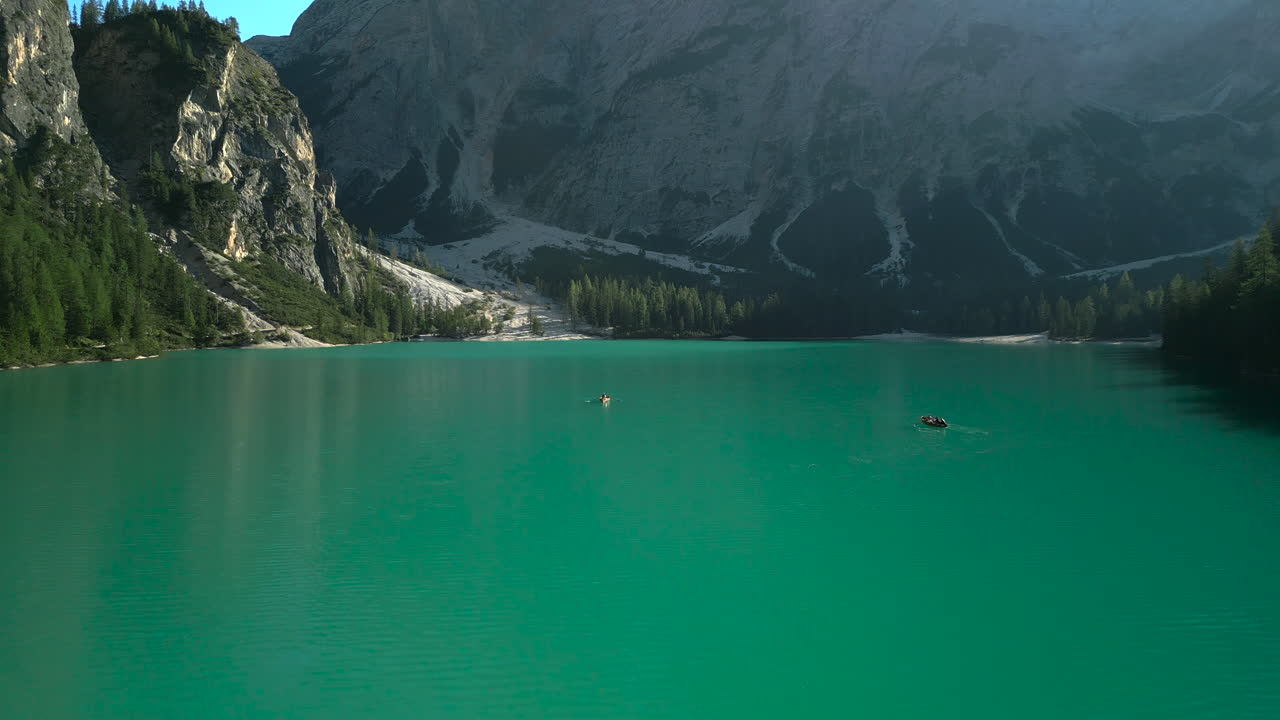 Passaggio aereo tra barche a remi sul Lago di Braies che cattura scogliere, montagne e ombre della foresta in una limpida mattinata. Planata veloce e bassa in avanti. 4K a Apple ProRes 25 fps.