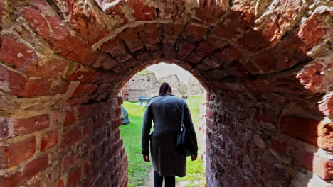 young woman walking through narrow walkway in bauska castle, back view