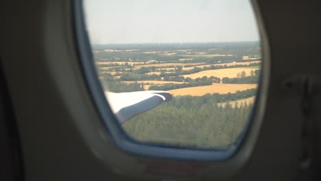 look out the window of a small private jet flying over fields.