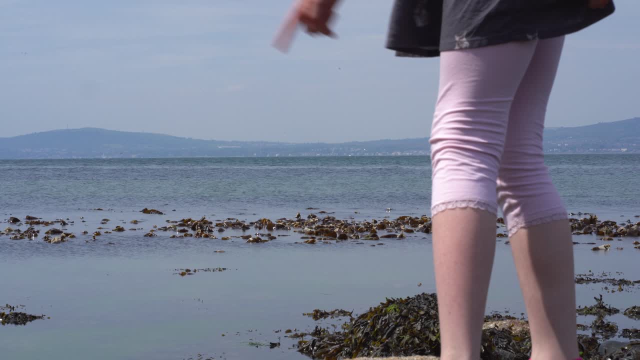 Young girl legs looking at sea and walking on rocks