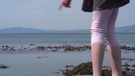 young girl legs looking at sea and walking on rocks