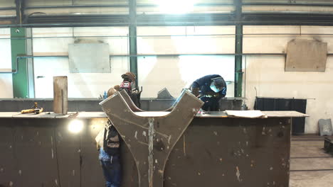 Workers-welding-big-steel-bridge-girder-beam-in-metal-factory-workshop