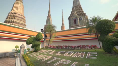 entrance to wat pho temple in bangkok, thailand, with lush greenery and traditional thai stupa architecture, establishing tilt up along grass to towers