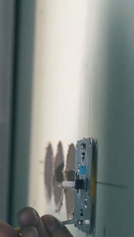 cu: skilled builder in plastic goggles installs plug on light green wall using screwdriver in repairing room close view
