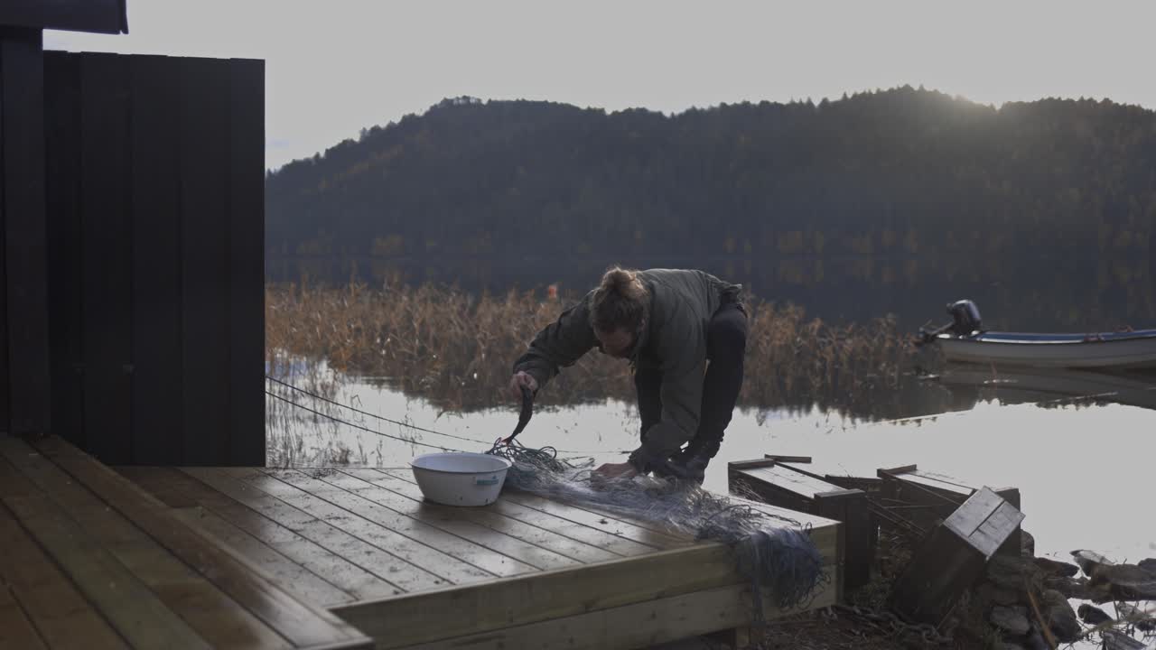 어부는 호수와 산을 배경으로 물고기를 분지에 넣습니다.