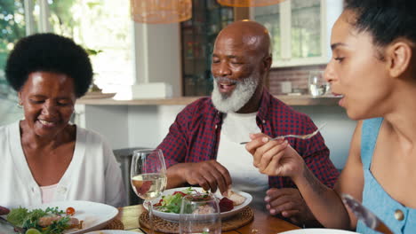 senior parents with adult offspring sitting around table eating meal at home together