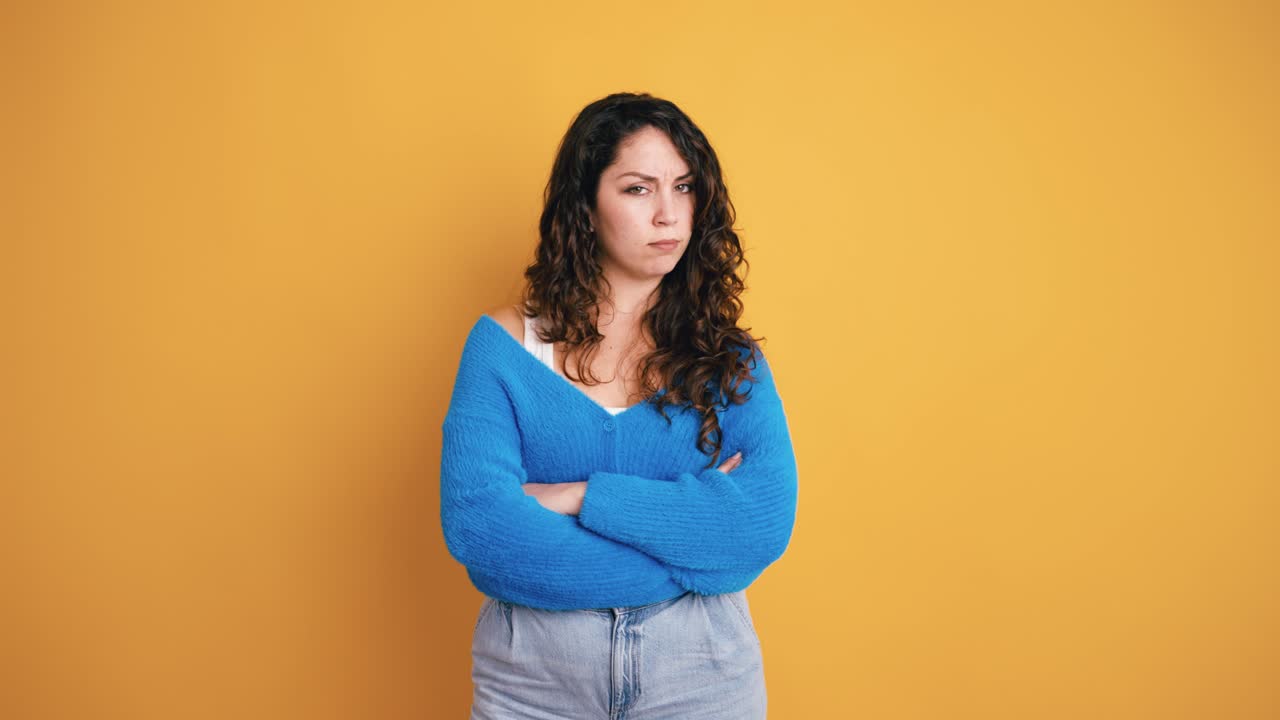 Annoyed Young Woman with Arms Crossed on Yellow Background