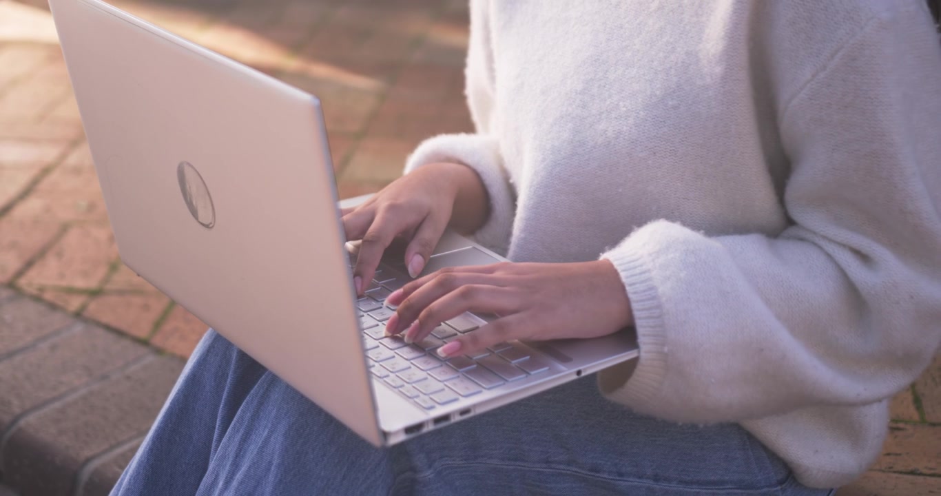 Bambina che alza le mani, digita con costanza su un portatile argentato in un patio, con un maglione morbido, mentre lavora