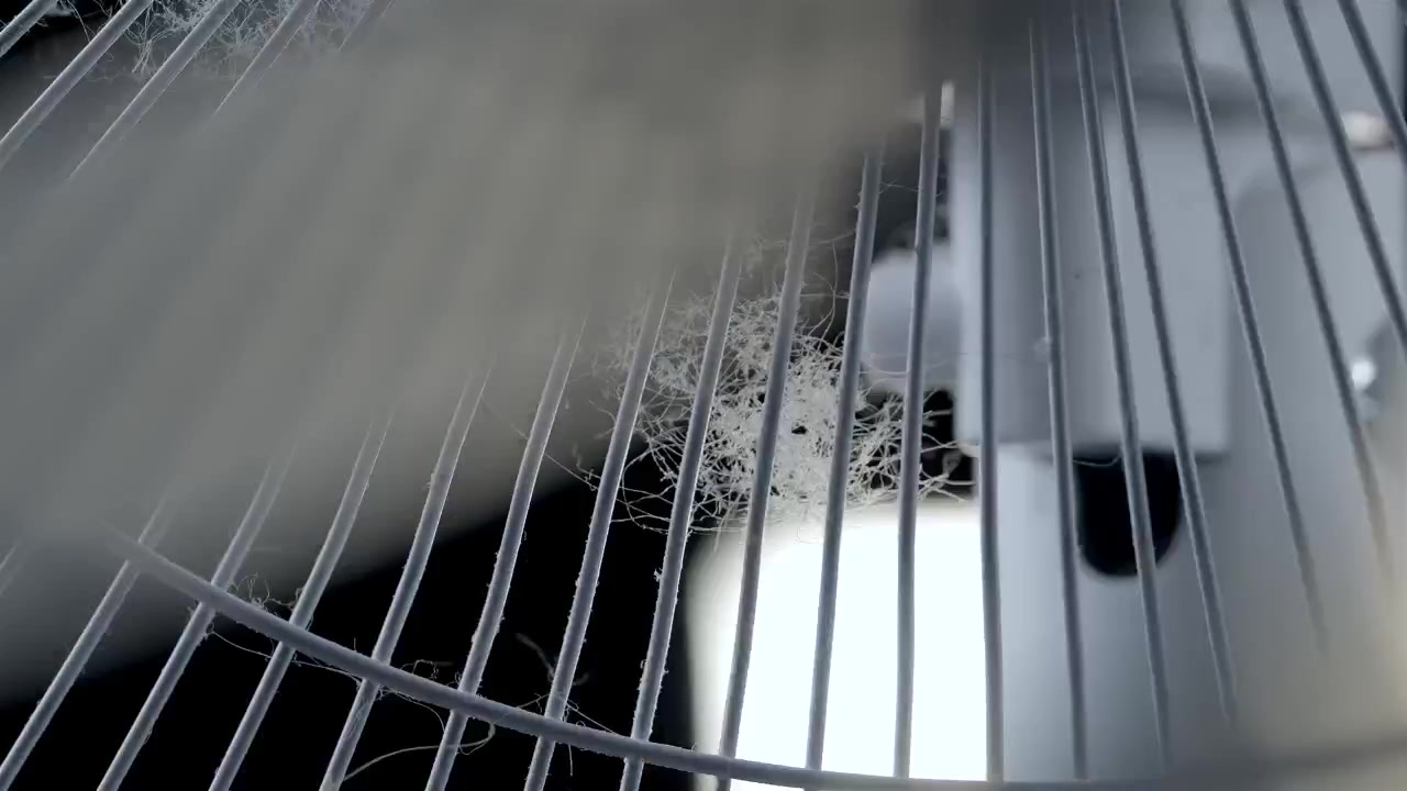 Uskarpe vifteblader beveger seg bak et støvete metallgitter i et nært interiørbilde.