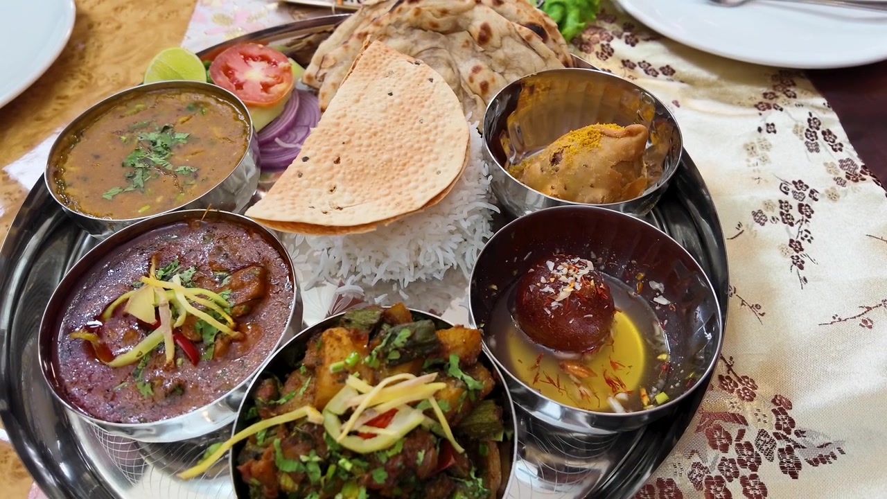 Overhead view of a diverse Indian vegetarian thali featuring curry, naan, and gulab jamun.