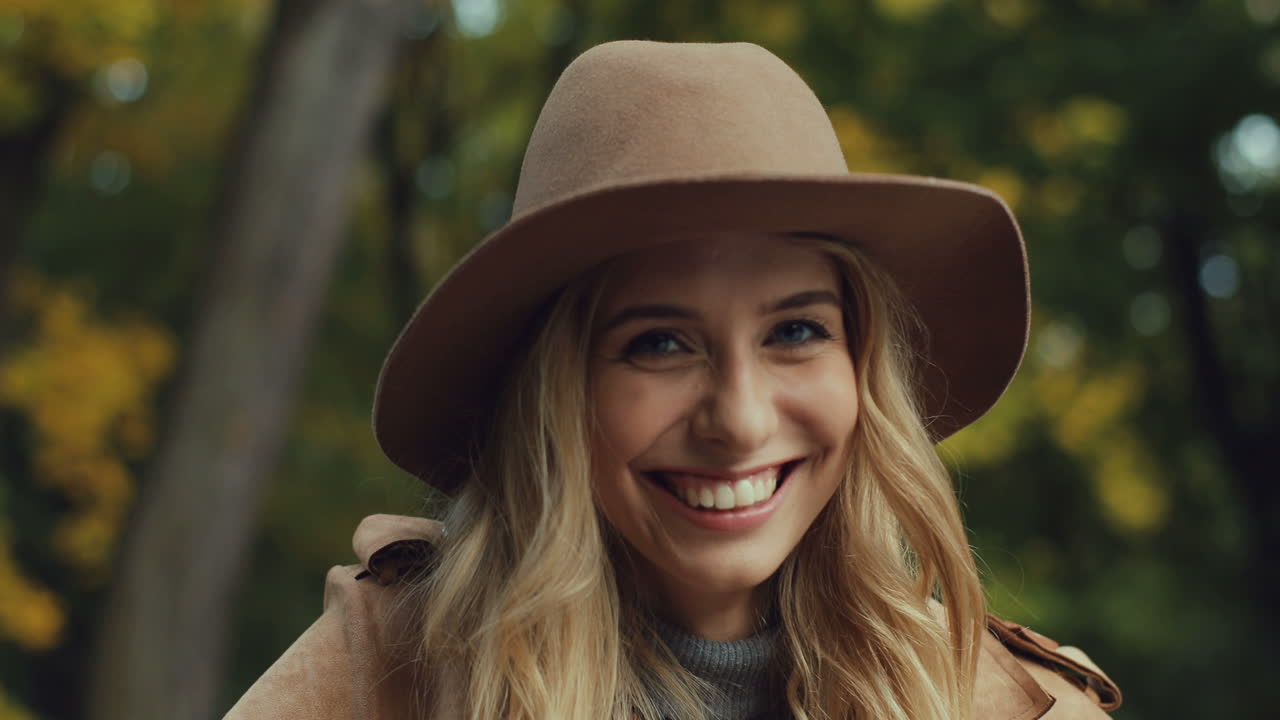 vista de cerca de una joven rubia caucásica con un sombrero riéndose y mirando la cámara en el parque en otoño