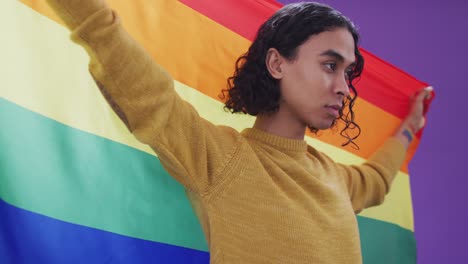 hombre biracial posando y sosteniendo la bandera lgbt con los brazos abiertos