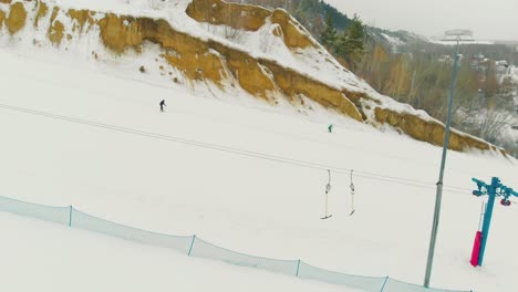 people ski down wide snowy trail with t-bar lift aerial view