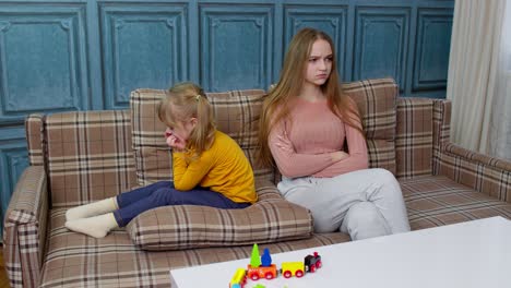 Unhappy-stressed-woman-and-angry-child-girl-sister-ignoring-each-other-sitting-on-sofa-after-quarrel