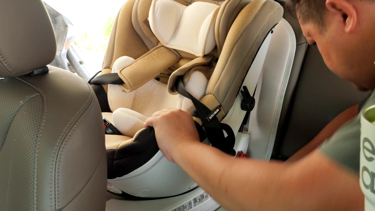 Un hombre revisa la instalación de una silla de coche para niños en el asiento trasero de un vehículo, asegurando un ajuste adecuado. Útil para guías de paternidad o demostraciones de seguridad.