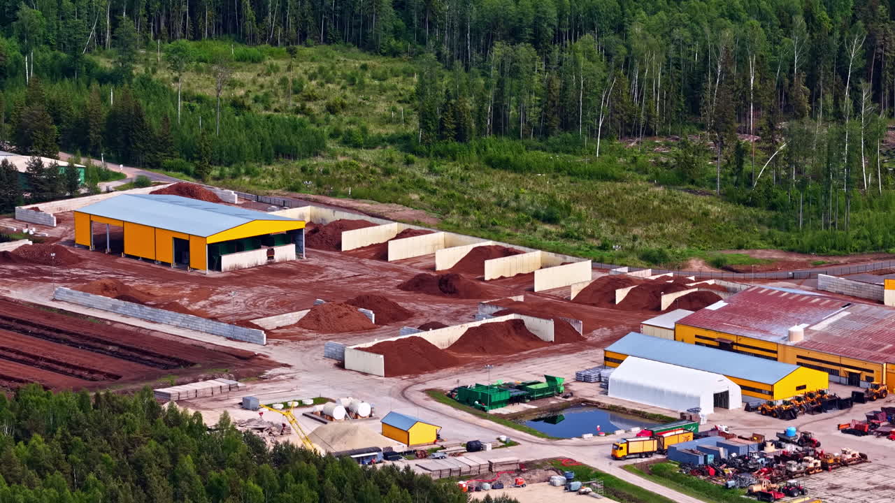 Peat processing factory with large piles of raw material and storage sections in forested area