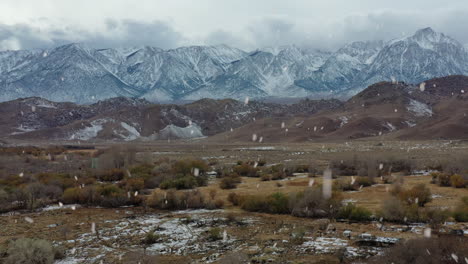 snow covered mountains and swampy landscape during snowfall, aerial ascend view