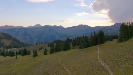 aerial flying over a hiking trail and tree lined ridge and towards a mountain range in the colorado rockies at sunset