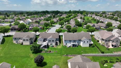 peaceful suburban neighborhood with green lawns, trees and modern family homes under a blue sky. ideal residential area with quiet streets and well-kept properties. aerial forward shot.