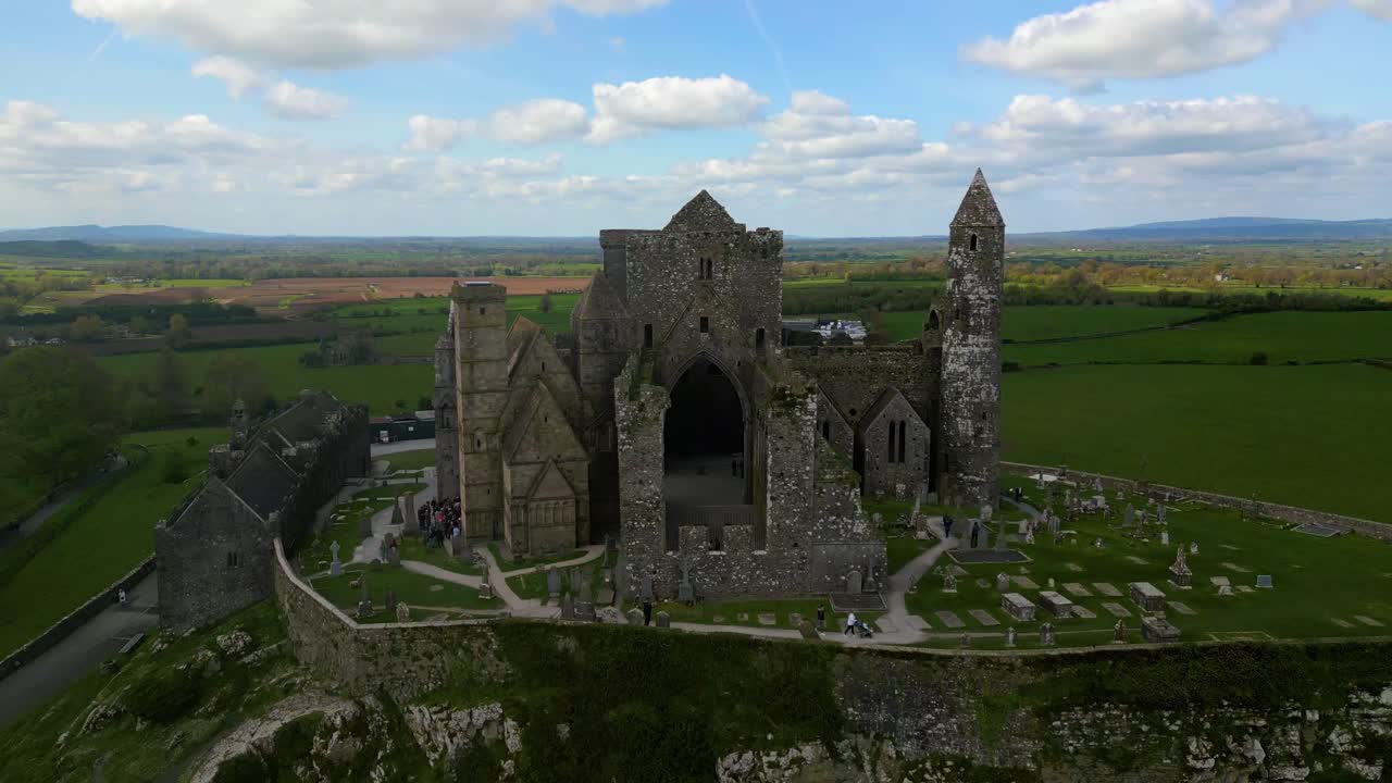 4K Aerial view of the Rock of Cashel, capturing ancient stone walls, round towers, and cathedral ruins surrounded by rolling green fields and historic farmland. Co.Tipperary, Ireland_015
