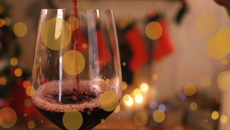 animation of glowing spots over glass of red wine and christmas decorations