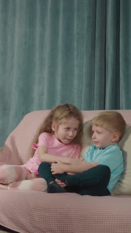 caring mother with paralysis sits in wheelchair reading fairytale for little children. curious girl and boy rest on pink sofa listening to mommy