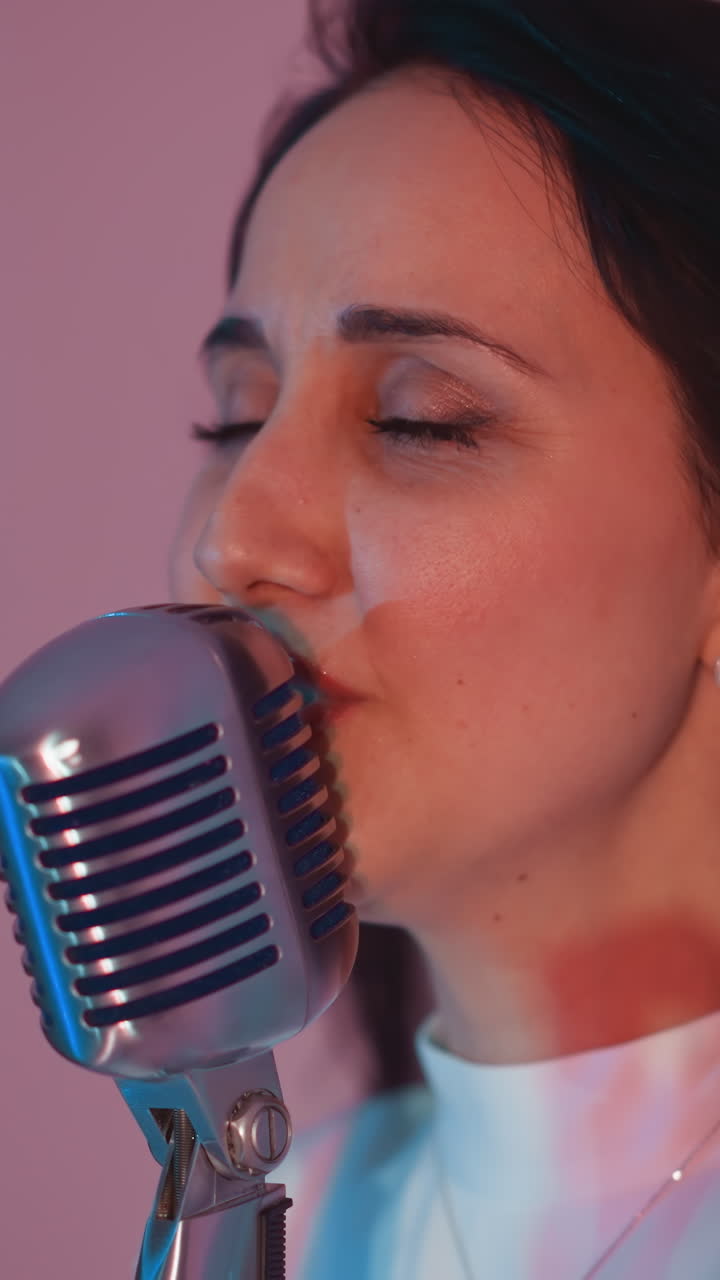 빈티지 마이크에 열정적으로 노래하는 가수의 측면 시각, 그녀의 머리카락이 흐릿한 분홍색 배경에 흐르고 있습니다.