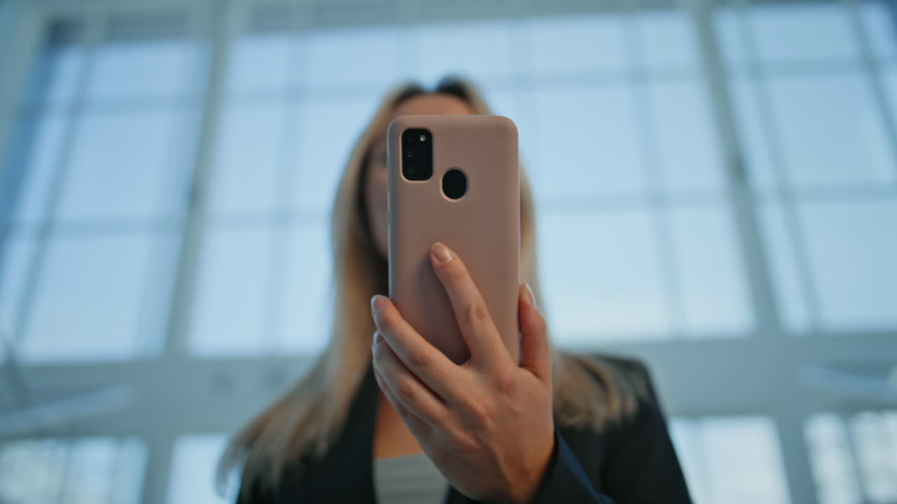 Donna in carriera che legge un SMS sullo smartphone in un ambiente aziendale, primo piano. Donna sorridente
