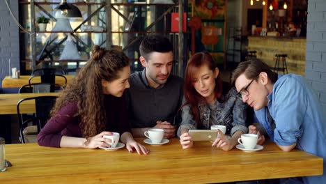 amigos guapos están viendo videos interesantes y discutiéndolo mientras beben té en la mesa en un acogedor café. estilo de vida moderno y concepto de gente feliz.