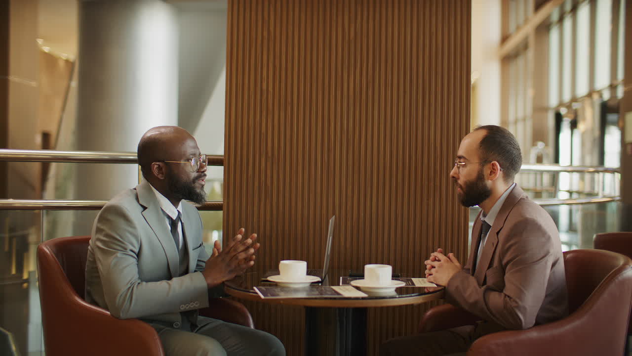 Two Business Partners Meeting and Discussing Project over Coffee in Hotel Lounge