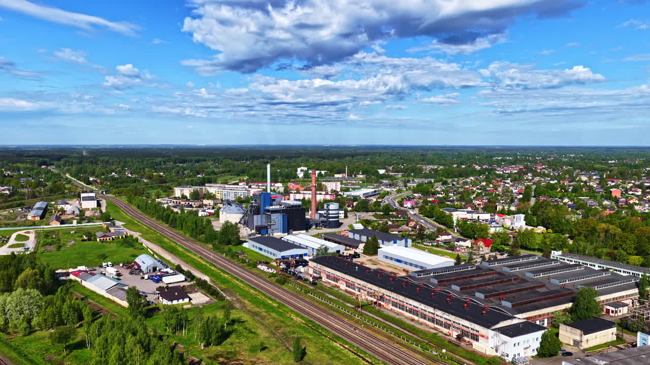 Industrial plant and rail lines next to green suburban neighborhood, clear sunny day