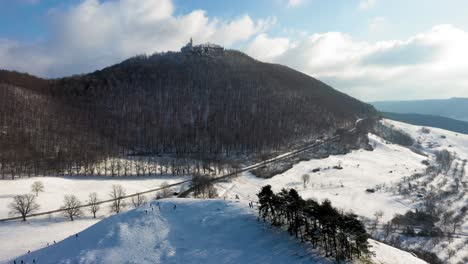 Aerial-helix-flying-over-winter-wonderland-alongside-mountains-and-sun-reflecting-in-camera-stunning-landscape-and-Castle-Teck-in-Swabia,-Germany