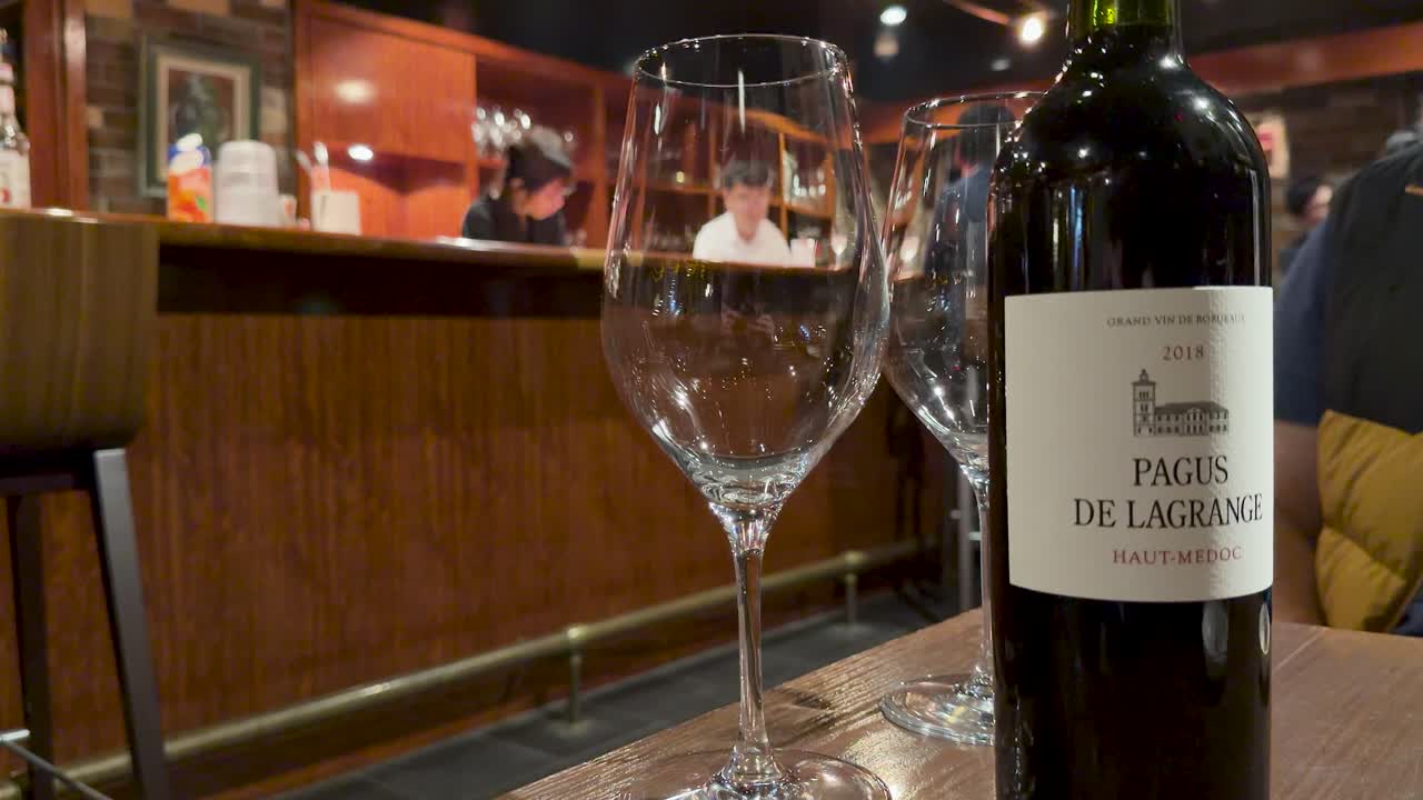 En flaske rødvin og tomme glass står på et bord i en svakt opplyst bar.