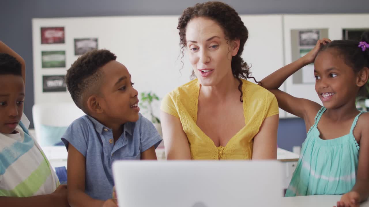 Video of happy caucasian female teacher and african american pupils using laptop