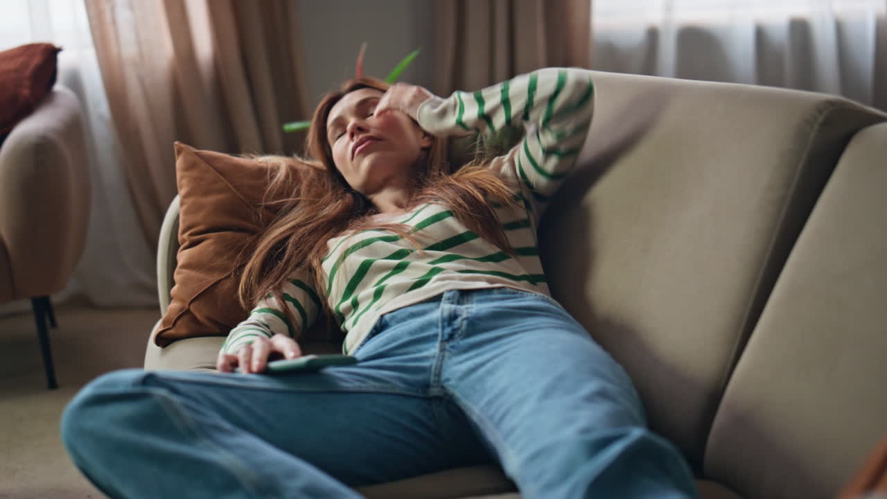 Sleepy woman resting couch holding mobile phone close up. Bored girl lying sofa