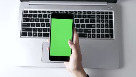 female hands swiping on the smartphone's touchscreen. green screen, chromakey concept, laptop in the background. top shot 60 fps