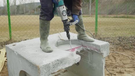 male worker builder uses electric impact drill to demolish precast concrete pits well slow motion