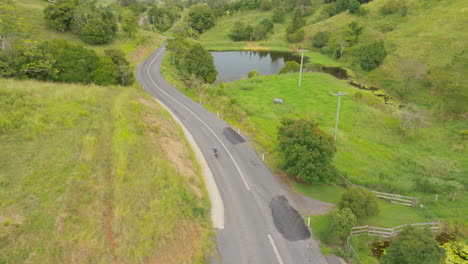 Athletic-Cyclist-Riding-Bike-Down-Scenic-Bush-Rural-Australian-Road,-4K-Drone-Slow-Motion