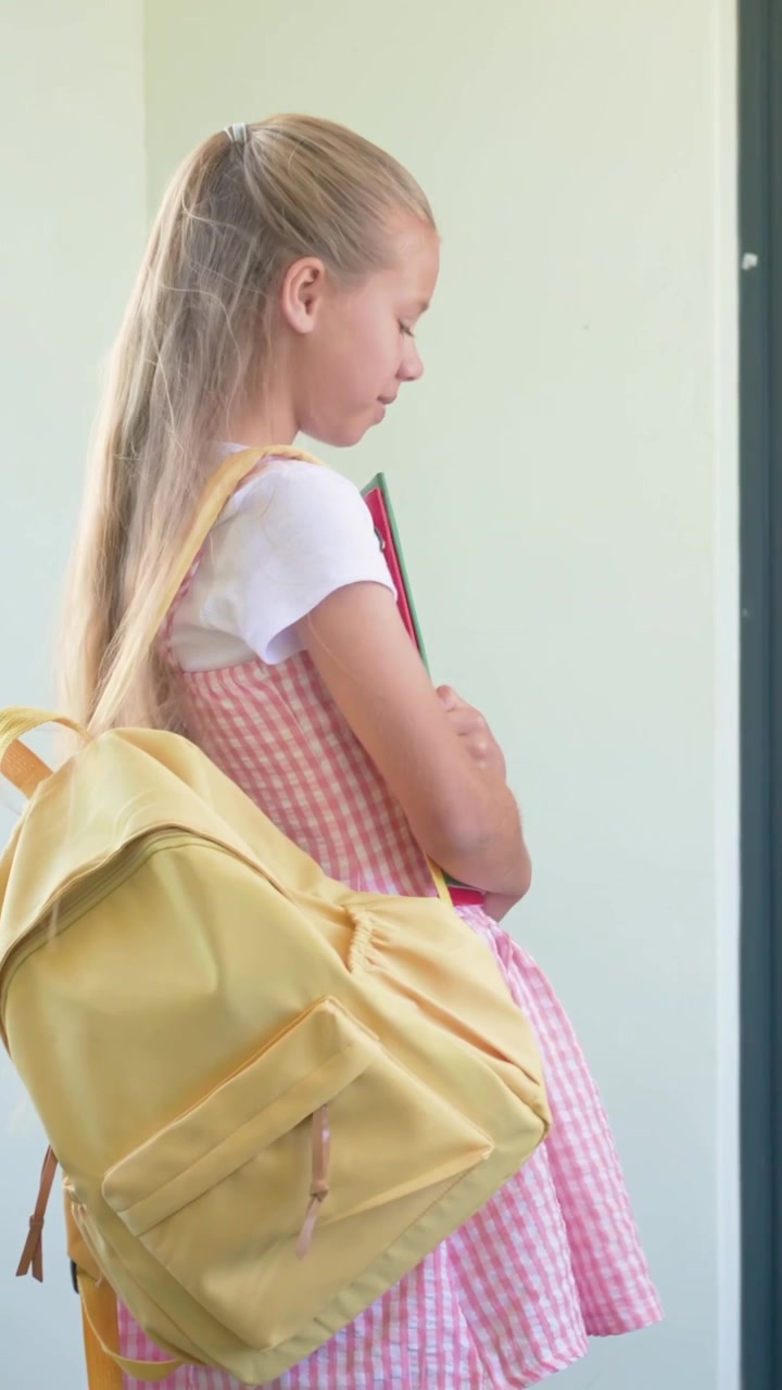 Vertical video: Entering hallway, camera following child in pink holding folders fixing yellow bag