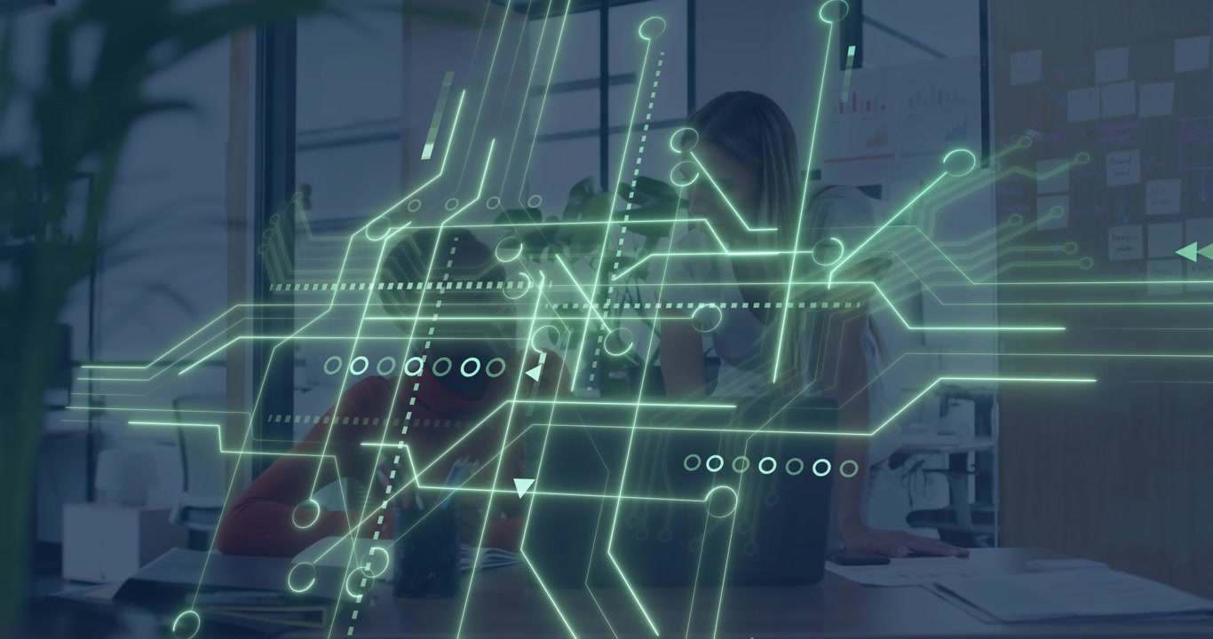 Two women collaborating at desk, animated green circuit sweeping revealing laptop for business task