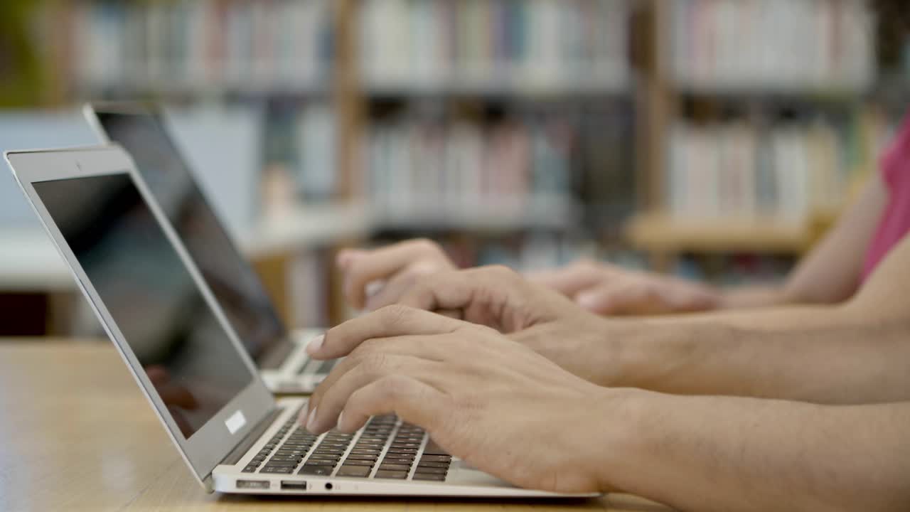 toma en cámara lenta de estudiantes escribiendo en computadoras portátiles en la biblioteca