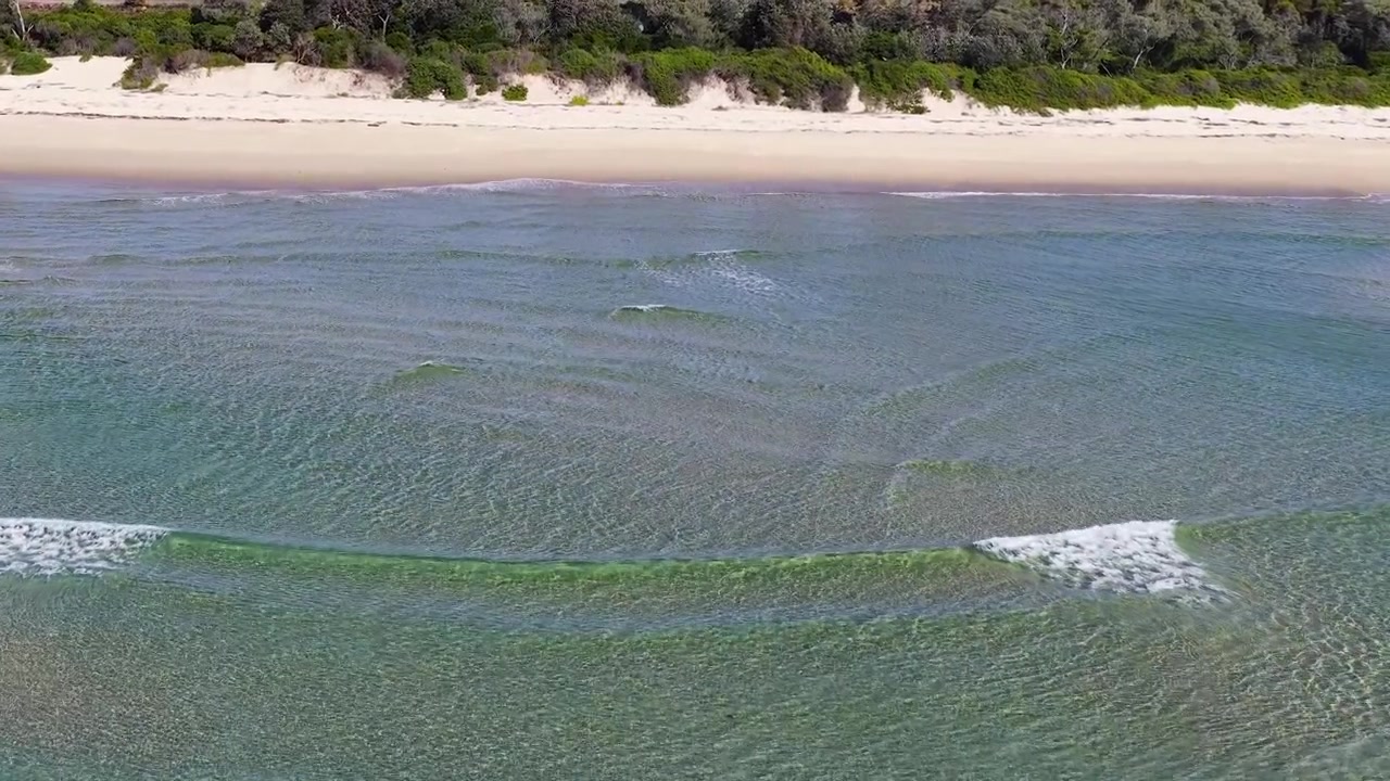 High-angle drone shot of turquoise ocean waves rolling onto sandy shoreline at South West Rocks.