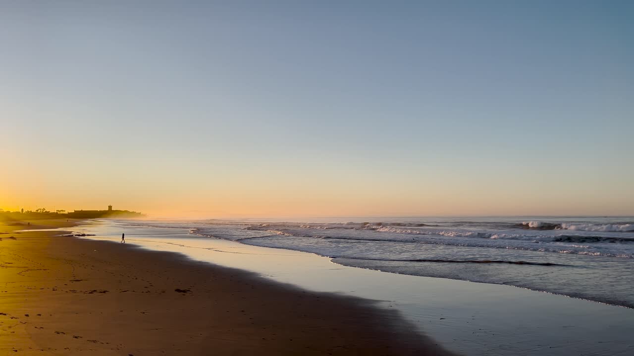 Panoramic view of man walking on a golden beach at sunset.
