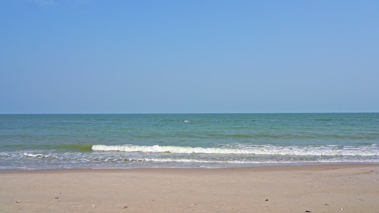 Slow motion, static shot of small waves breaking on sandy beach at midday