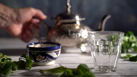 slow motion tight shot of hand picking up an ornate teapot and pours tea into a glass with moroccan bowl and mint around