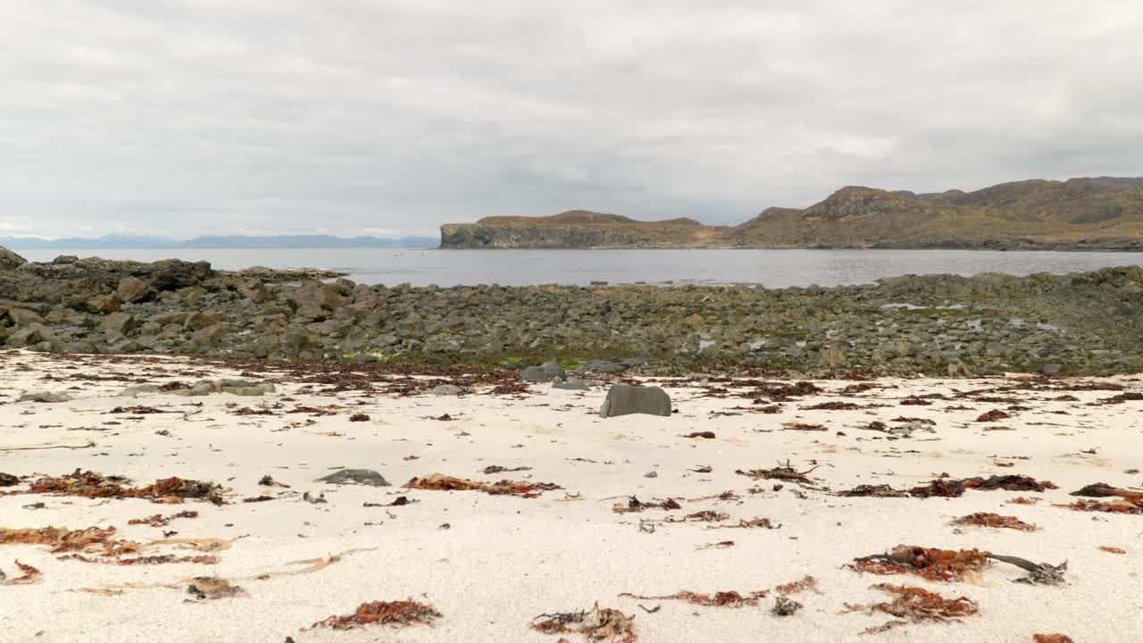 медленная съемка с панорамированием вдоль песчаного пляжа в шотландии с видом на валуны, океан и горы на заднем плане