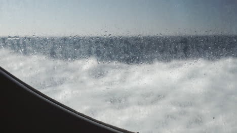 water mist on ship porthole window as it travels on ocean, waves in background, slow motion
