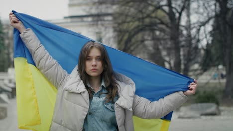 mujer caucásica sosteniendo bandera ucraniana estirada y mirando a la cámara.